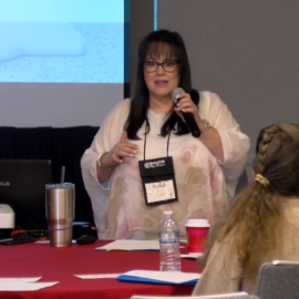 A woman standing at a table with a microphone.