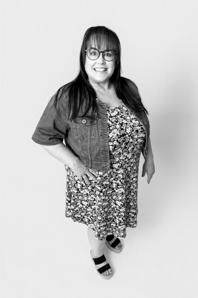 Woman smiling in floral dress and glasses.