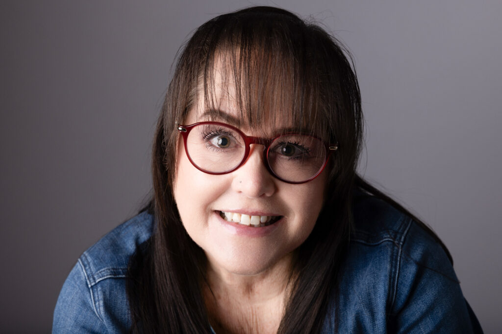 Smiling person with glasses and brown hair.